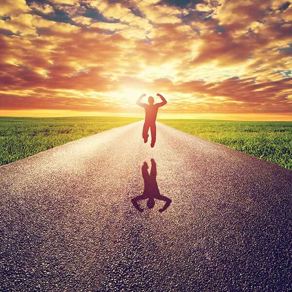 A man hopping on a road with a sunny sky and green grass growing around him.