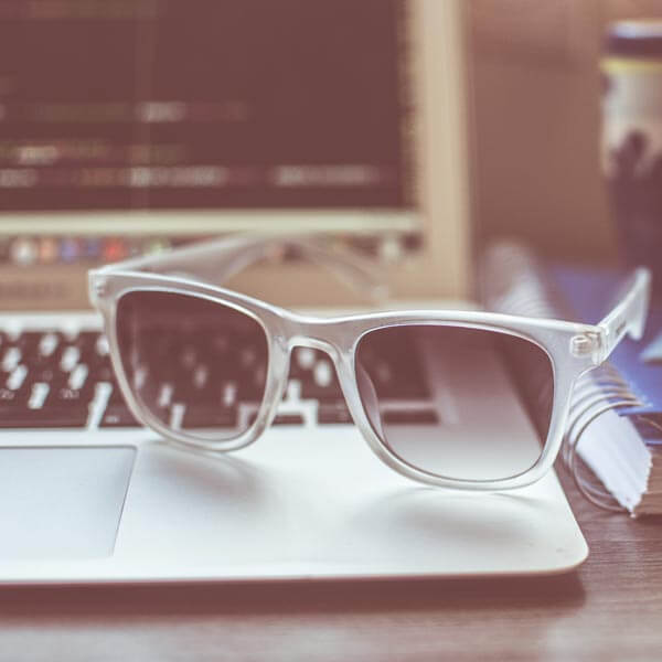 A laptop with sunglasses resting on the keyboard with clear frames and lightly tinted shades.