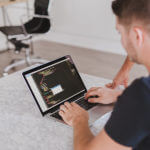 A professional man wearing a black shirt working on a line of code on his laptop.