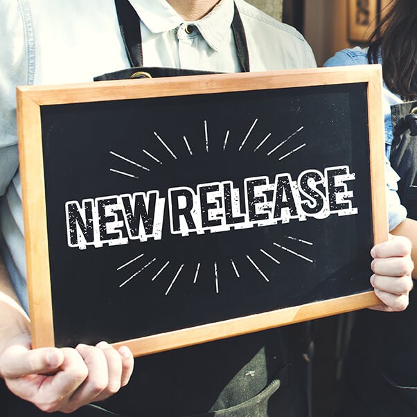 A man wearing an thick apron and a collard shirt holding a new chalk sign with the saying new release on it.
