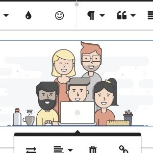 A group of working professionals gathered around one man working on a laptop with text editing tools around them.