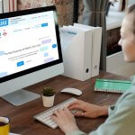A woman working on an iMac displaying the Froala WYSIWYG HTML editor's website.