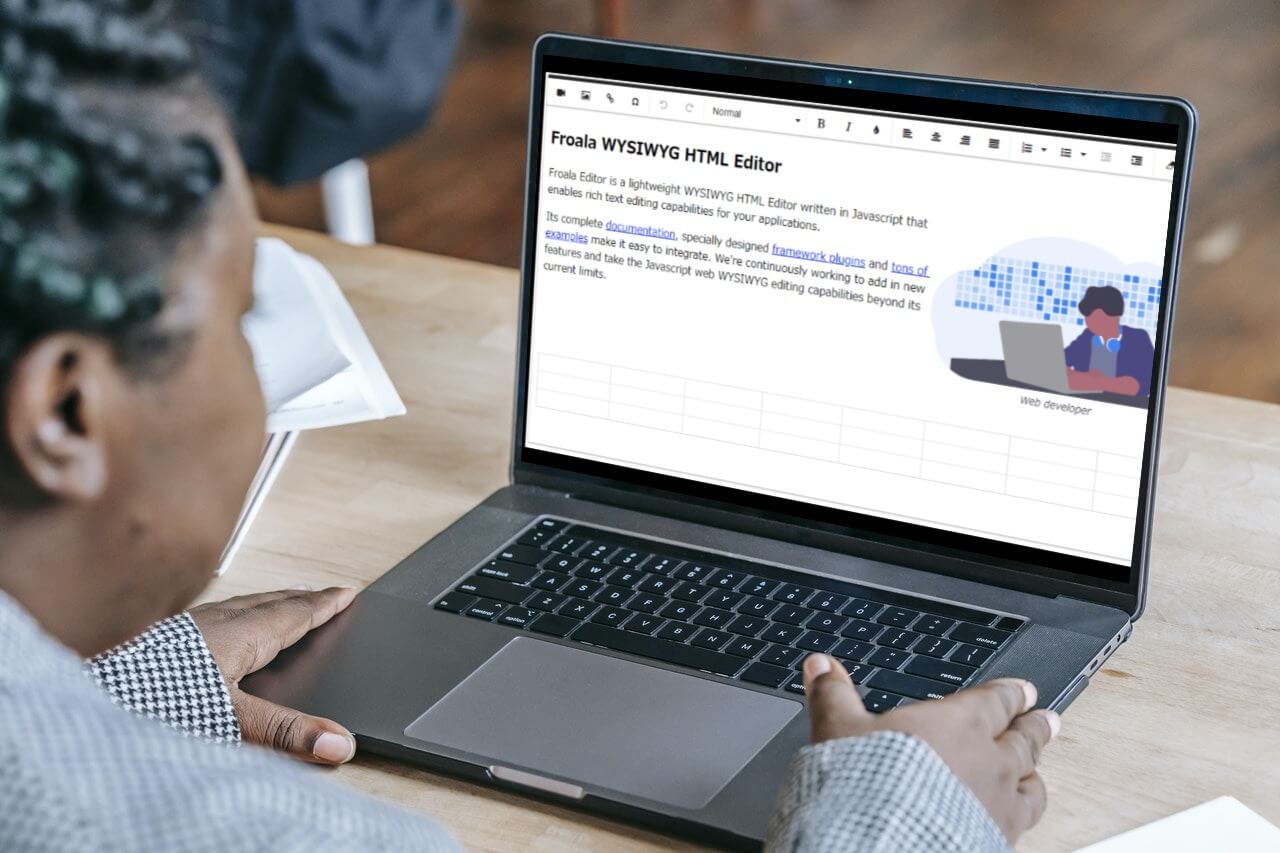 A person using a laptop with the Froala WYSIWYG HTML Editor on the screen.